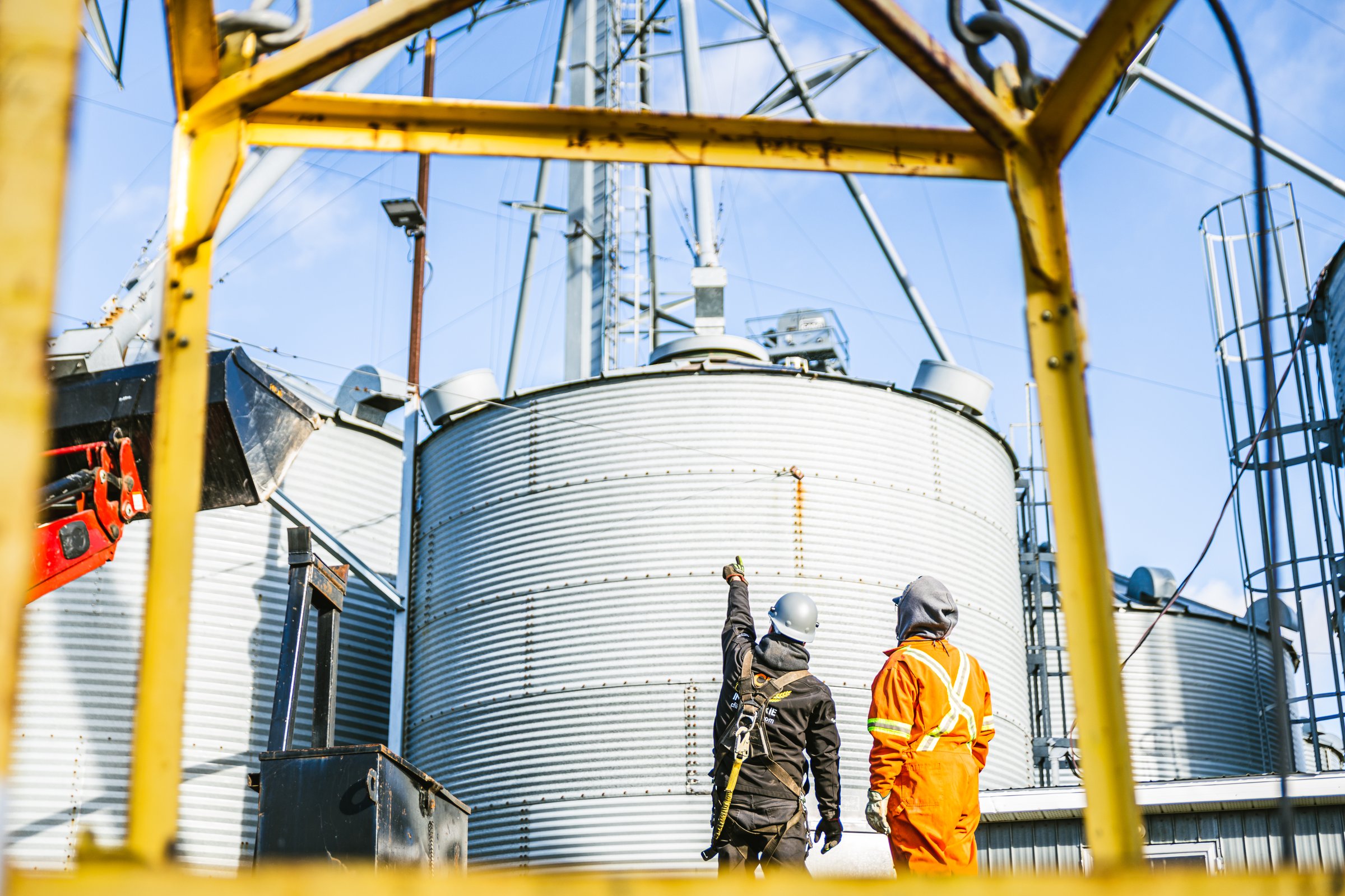 CFI Industries crew in technical discussion at grain silo installation — industrial mechanics with safety harnesses and PPE, intervention in Saguenay–Lac-Saint-Jean